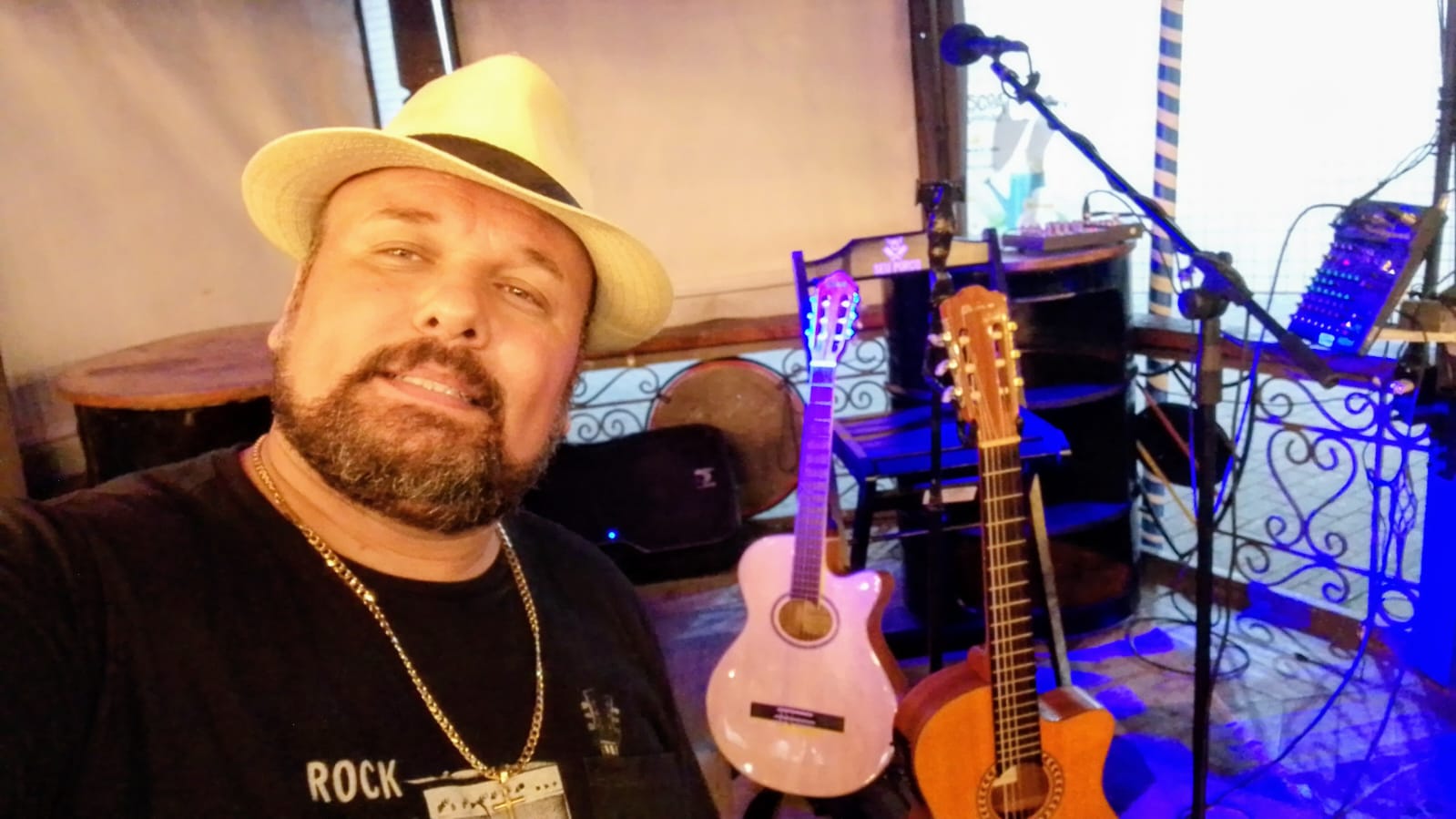 Paulinho Monteiro de chapéu, ao lado dos violões e do microfone no espaço de apresentação